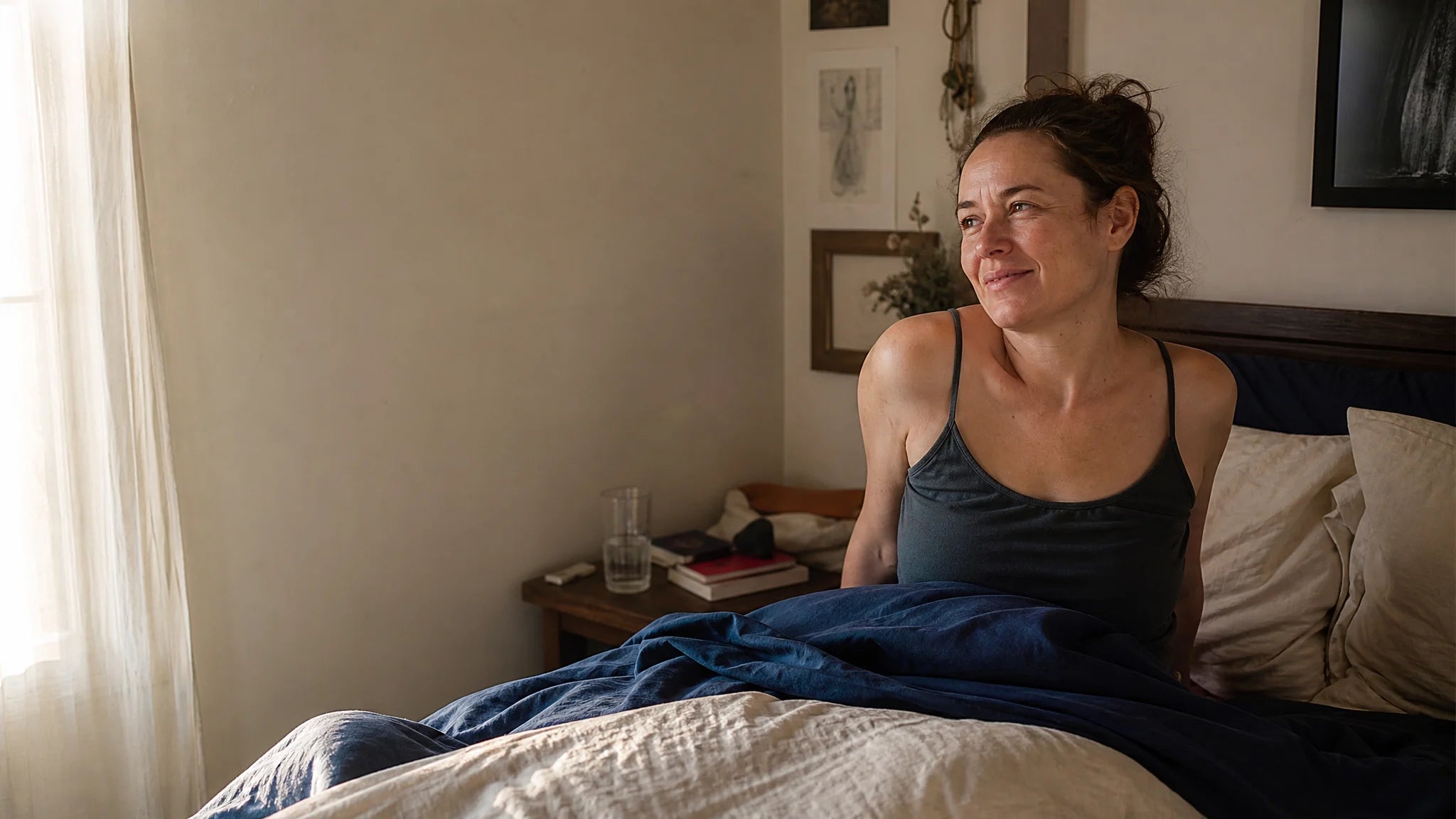 A woman sitting up in bed at dawn, rested